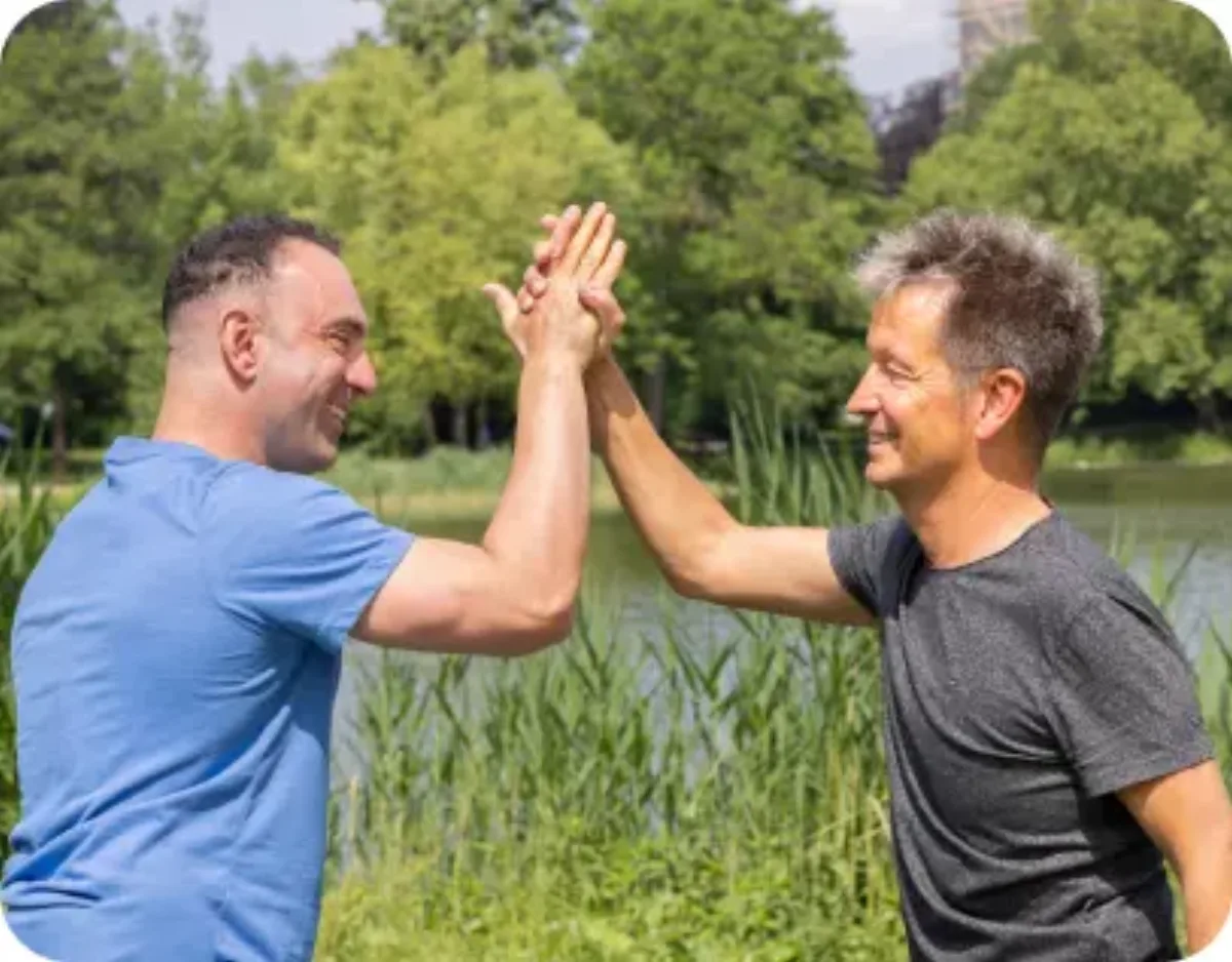 Zwei Männer geben sich im Park am Wasser ein High-Five