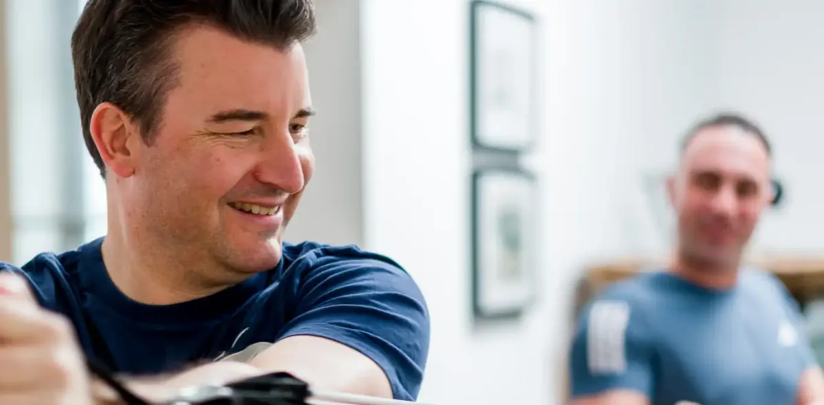 Ein Kunde trainiert an einem Fitnessgerät, Nico Fichtler im Hintergrund
